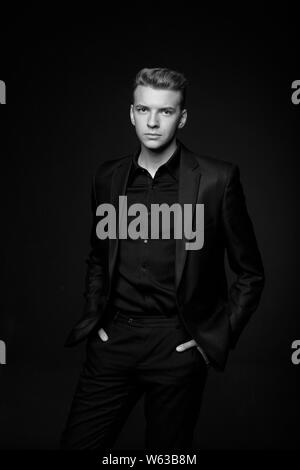 Jeune homme en veste noire sur fond noir, noir et blanc Banque D'Images