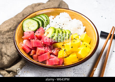 Bol de riz avec du thon poke, avocat, mangue et concombre sur tableau blanc. Banque D'Images