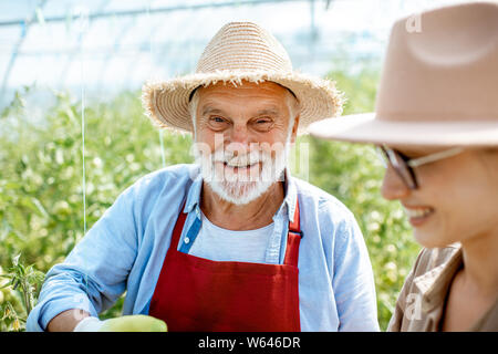 Portraiit d'un grand-père heureux avec jeune femme dans le contexte compétitif d'une petite ferme agricole avec plantation de tomate Banque D'Images