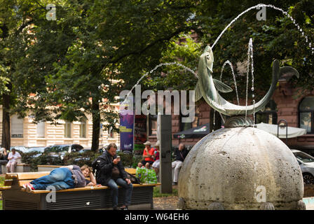 Fontaine avec des poissons et des gens sur un banc dans l'arrière-plan, Mainz, Allemagne Banque D'Images