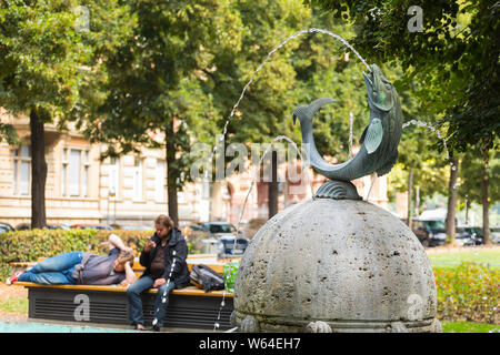 Fontaine avec des poissons et des gens sur un banc dans l'arrière-plan, Mainz, Allemagne Banque D'Images