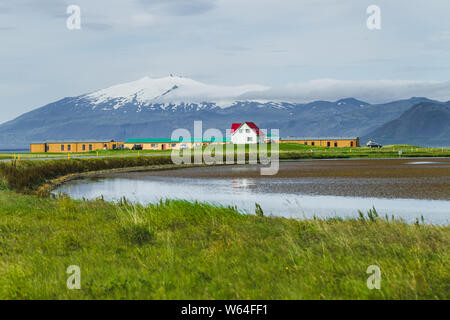 Paysage de campagne traditionnelle islandaise. Maison blanche au toit rouge. Une maison solitaire sur vert prairie avec vue sur la montagne avec un sommet enneigé. Banque D'Images