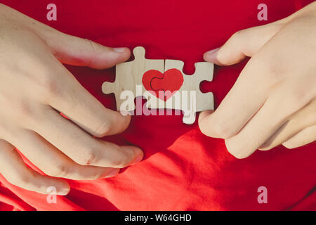 Coeur rouge est dessiné sur les pièces du puzzle dans les mains sur fond rouge. Concept d'amour. Jour de la Saint-Valentin Banque D'Images