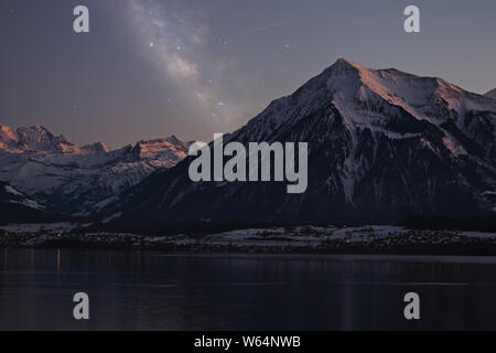 Voie lactée au-dessus du lac de Thoune et le Niesen mountain pendant le crépuscule illuminant les montagnes enneigées avec rose. Banque D'Images