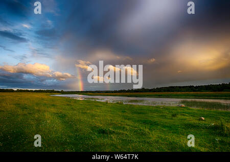 Beau paysage d'été avec double arc-en-ciel dans ciel dramatique au-dessus de la rivière entre les vertes prairies Banque D'Images