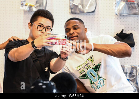 Star de la NBA Russell Westbrook des Oklahoma City Thunder, droite, avec un ventilateur autoportraits prend à un fan meeting événement au cours de sa visite en Chine à Shanghai, Chine, Banque D'Images