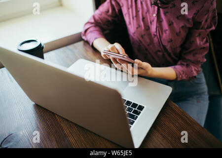 Travail féminin avec téléphone mobile et ordinateur portable, tasse de café sur la table en bois à côté. Vue d'en haut. Banque D'Images