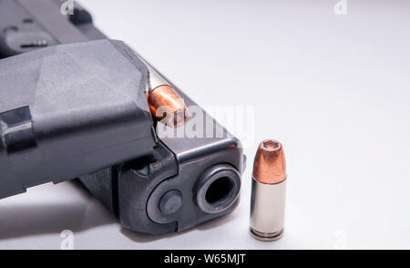 Noir un pistolet 9 mm avec un chargeur plein au-dessus et une seule balle à pointe creuse de 9 mm à côté de lui sur un fond blanc Banque D'Images