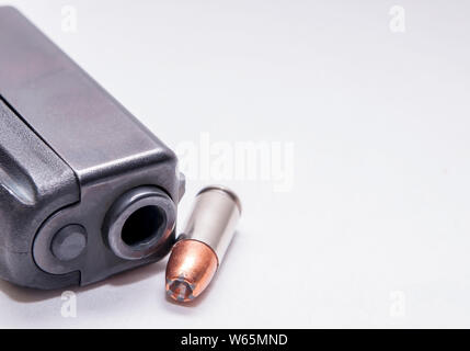 Un pistolet 9 mm noir museau avec une seule balle à pointe creuse de 9 mm à côté de lui sur un fond blanc Banque D'Images