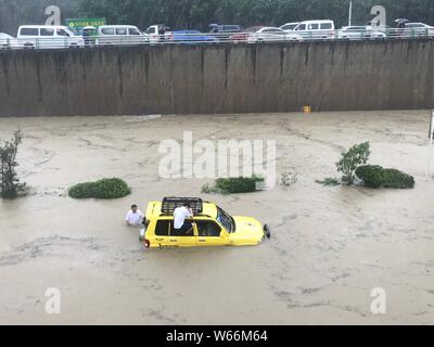 Les résidents de pousser une voiture piégée dans une route inondée causées par de fortes pluies dans la ville de Chengdu, dans le sud-ouest de la province chinoise du Sichuan, le 11 juillet 2018. Fl Banque D'Images