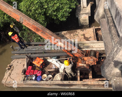 Équipe de travailleurs tirez des colonnes de béton hors de l'eau sur le fer avec ponton grue. La reconstruction de la côte du fleuve, Thaïlande Banque D'Images