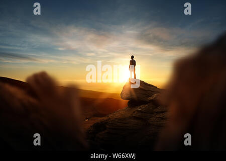 Leadership et objectifs. Un homme standning au sommet d'une montagne regardant le coucher de soleil. Photo conceptuelle composite. Banque D'Images