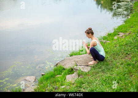 Jeune fille brune mince yogi ne difficile les exercices de yoga sur l'herbe verte sur le fond de l'eau. Banque D'Images