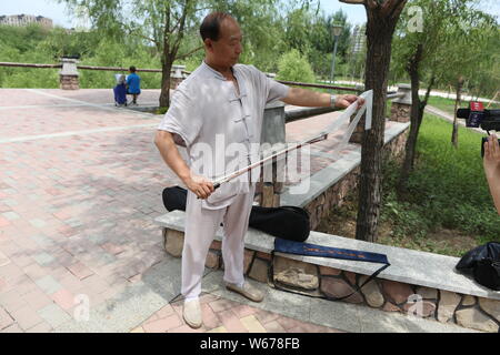 61 ans, ancien musicien chinois Liang Linsheng erhu joue un arc le long du bord d'une scie pour créer des sons et de la musique à un parc dans la ville de Jilin, nort Banque D'Images