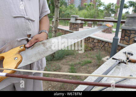 61 ans, ancien musicien chinois Liang Linsheng montre un archet erhu et une scie à bois qu'il utilise pour créer des sons et de la musique à un parc dans la ville de Jilin, nord Banque D'Images