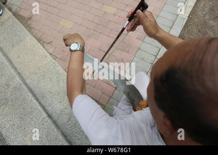 61 ans, ancien musicien chinois Liang Linsheng erhu joue un arc le long du bord d'une scie pour créer des sons et de la musique à un parc dans la ville de Jilin, nort Banque D'Images