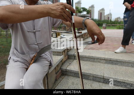 61 ans, ancien musicien chinois Liang Linsheng erhu joue un arc le long du bord d'une scie pour créer des sons et de la musique à un parc dans la ville de Jilin, nort Banque D'Images