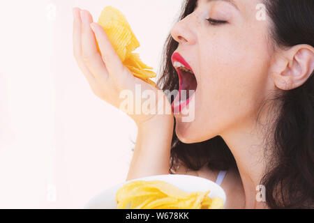 Jolie jeune fille affamée mange beaucoup de frites, est titulaire d'une poignée d'en-cas et le met dans la bouche. Close-up portrait of a Girl mange goulûment Français Banque D'Images