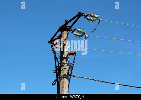 Poteau de béton avec plusieurs fils électriques connectés avec isolateurs en céramique et en verre clair sur fond de ciel bleu Banque D'Images