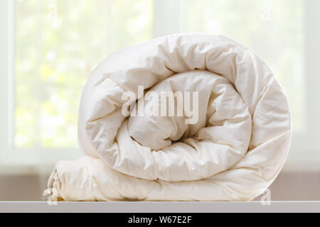 Une couette pliée rouleaux est couchée sur la commode dans le contexte d'une vitre brouillée. Ménage. Banque D'Images
