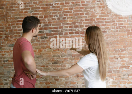 Jeune couple vacances ensemble de réparation eux-mêmes. L'homme et de la femme mariés faisant Home makeover ou rénovation. Concept de relations, la famille, l'amour. Discuter de la peinture du mur ou le préparer pour. Banque D'Images