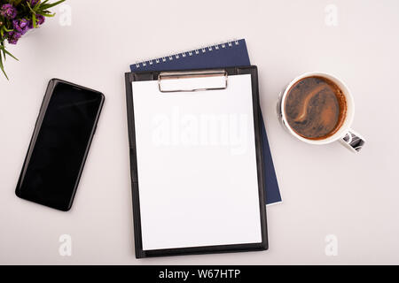 Planner sur la table de travail avec téléphone gris et du café. Papier blanc vierge sur un bureau de travail Banque D'Images