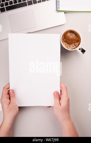 Man's hands holding le papier blanc sur le bureau de travail avec ordinateur et café Banque D'Images