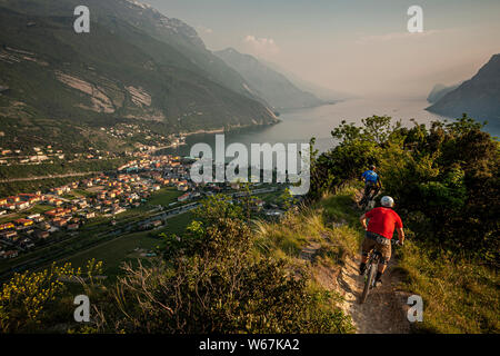 Le lac de Garde, Italie. Deux cyclistes de montagne équitation le long d'une voie unique étroite menant vers la ville de Riva del Garda. Soir lumière et brume sur Banque D'Images