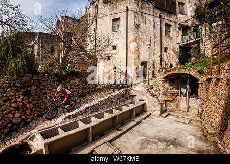 FINALE LIGURE, ITALIE. Deux cyclistes de montagne équitation sur une étroite rue pavée italienne avec un lave-linge. Banque D'Images