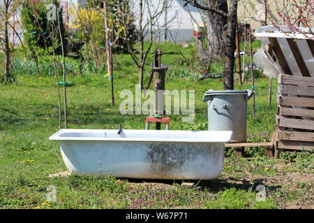 Vintage Retro old rusted côté pompe à eau avec baignoire utilisé comme réservoir d'eau en milieu urbain local jardin entouré d'herbe et de plantes de jardin Banque D'Images