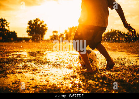 L'extérieur de l'action sport kids playing soccer le football pour faire de l'exercice en zone rurale communautaire sous le coucher du soleil au crépuscule. Pauvres et la pauvreté des enfants. Banque D'Images