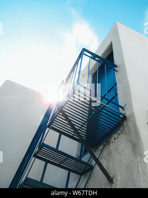 Prise de vue à angle bas de l'escalier bleu menant à un porte bleue avec le soleil brillant dans le ciel bleu Banque D'Images