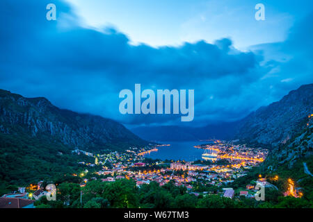 Monenegro, vue au-dessus de maisons, les rues et le port de la baie de Kotor ville entourée de montagnes et d'arbres après le coucher du soleil dans l'atmosphère crépusculaire d'enseignes lumineuses Banque D'Images