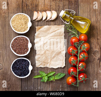 Variété de riz dans des bols, de l'huile d'olive, d'herbes et de légumes sur une table en bois et de vieux papier Banque D'Images