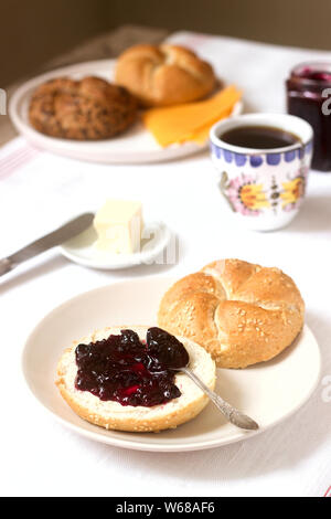 Petit-déjeuner avec petits pains Kaiser, confiture de cassis, beurre, fromage et thé. Banque D'Images