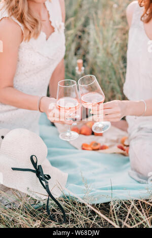 Les mains de deux femmes tenant deux verres de vin rose sur le coucher du soleil pique-nique. Rognées. Banque D'Images