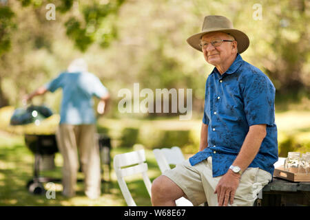 Happy homme assis sur une table de pique-nique dans un parc. Banque D'Images