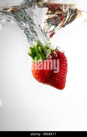 Une seule fraise chutes dans l'eau créant une belle bulle d'air comme il le fait. L'eau se trouve sur un fond blanc. Banque D'Images