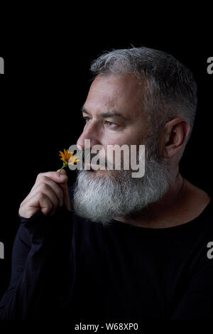 Portrait d'homme aux cheveux gris brutal avec une barbe d'essence de fleurs jaunes sur fond noir, selective focus Banque D'Images