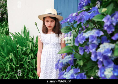 Jeune fille en robe blanche rester près de old cottage avec couleur bleu porte. Bright Hortensia à fleurs bleu trouble. Banque D'Images