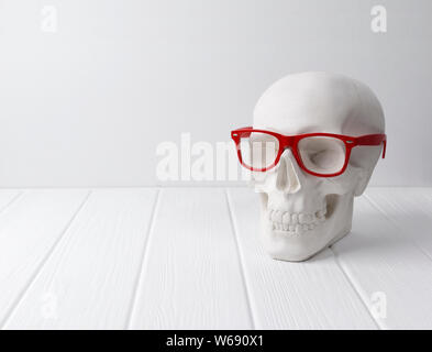 Crâne humain de gypse en rouge lunettes à la table en bois blanc. La science médico-légale et d'anatomie concept. Banque D'Images