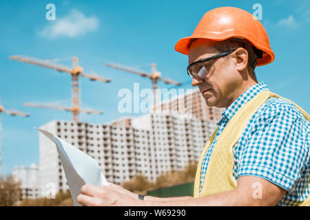 Homme constructeur, architecte ou ingénieur dans un casque et lunettes de sécurité sur un chantier de construction. Banque D'Images