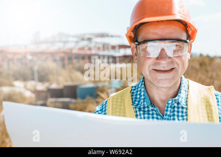 Homme constructeur, architecte ou ingénieur dans un casque et lunettes de sécurité sur un chantier de construction. Banque D'Images