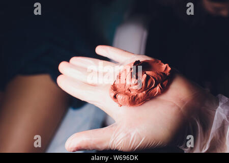 Une femme fait un masque d'argile cosmétique pour la peau saine. Dans ses mains une tasse et un bâton en remuant. Banque D'Images