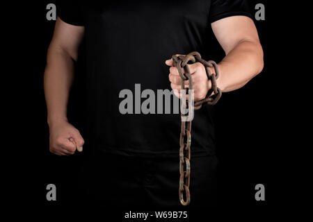 Homme adulte de noir se tient debout avec les muscles tendus et est titulaire d'une chaîne en métal rouillé, notion de force et d'endurance Banque D'Images