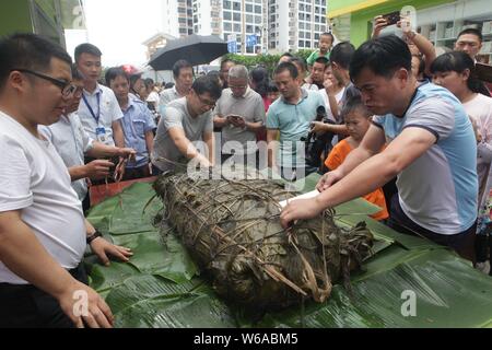 Les citoyens partagent un énorme zongzi, une boulette en forme de pyramide fait de riz gluant enveloppé dans des feuilles de roseau ou de bambou dans la ville de Liuzhou, Guangxi en Chine du sud Banque D'Images