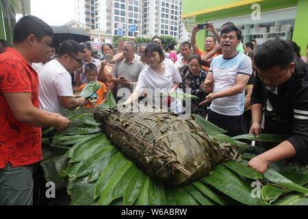 Les citoyens partagent un énorme zongzi, une boulette en forme de pyramide fait de riz gluant enveloppé dans des feuilles de roseau ou de bambou dans la ville de Liuzhou, Guangxi en Chine du sud Banque D'Images