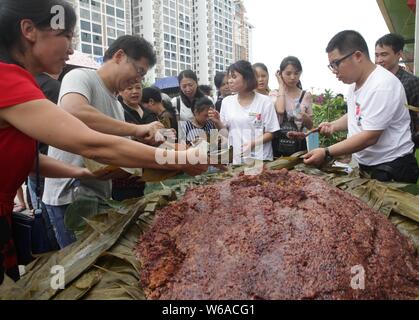 Les citoyens partagent un énorme zongzi, une boulette en forme de pyramide fait de riz gluant enveloppé dans des feuilles de roseau ou de bambou dans la ville de Liuzhou, Guangxi en Chine du sud Banque D'Images