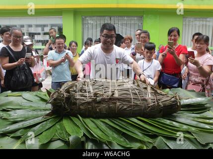 Les citoyens partagent un énorme zongzi, une boulette en forme de pyramide fait de riz gluant enveloppé dans des feuilles de roseau ou de bambou dans la ville de Liuzhou, Guangxi en Chine du sud Banque D'Images