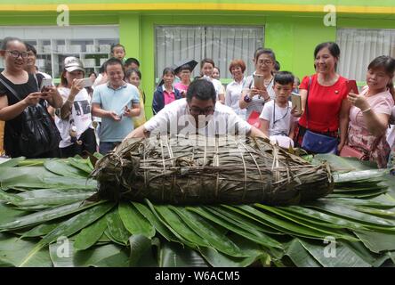 Les citoyens partagent un énorme zongzi, une boulette en forme de pyramide fait de riz gluant enveloppé dans des feuilles de roseau ou de bambou dans la ville de Liuzhou, Guangxi en Chine du sud Banque D'Images